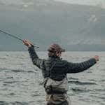 An adult man in waders fly fishing in a serene mountain lake.